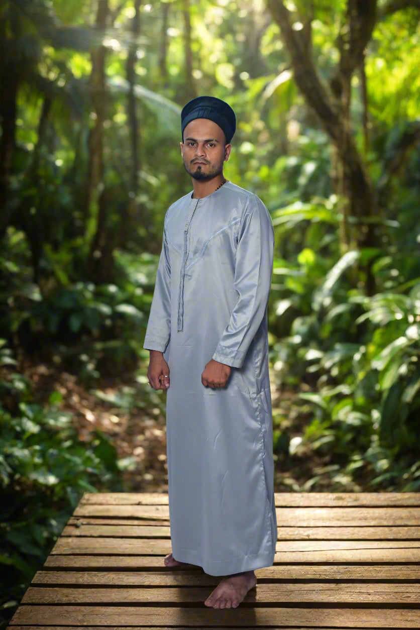 Man wearing a light gray traditional outfit with a black cap on a white background